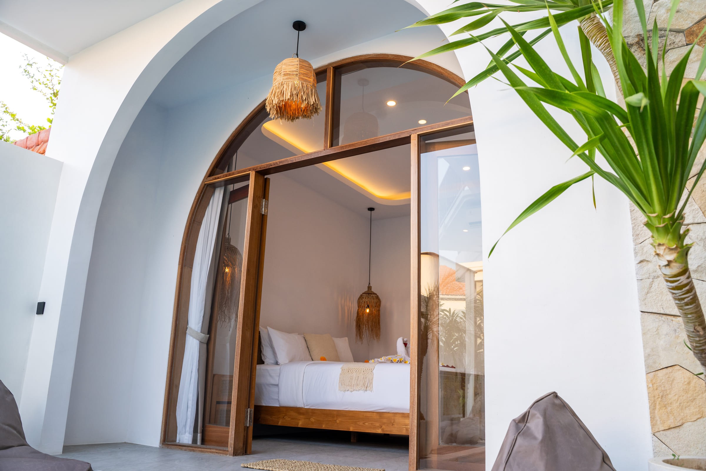 Arched glass doors opening into Bedroom One at Casa Aurea, with a woven pendant lamp above the bed