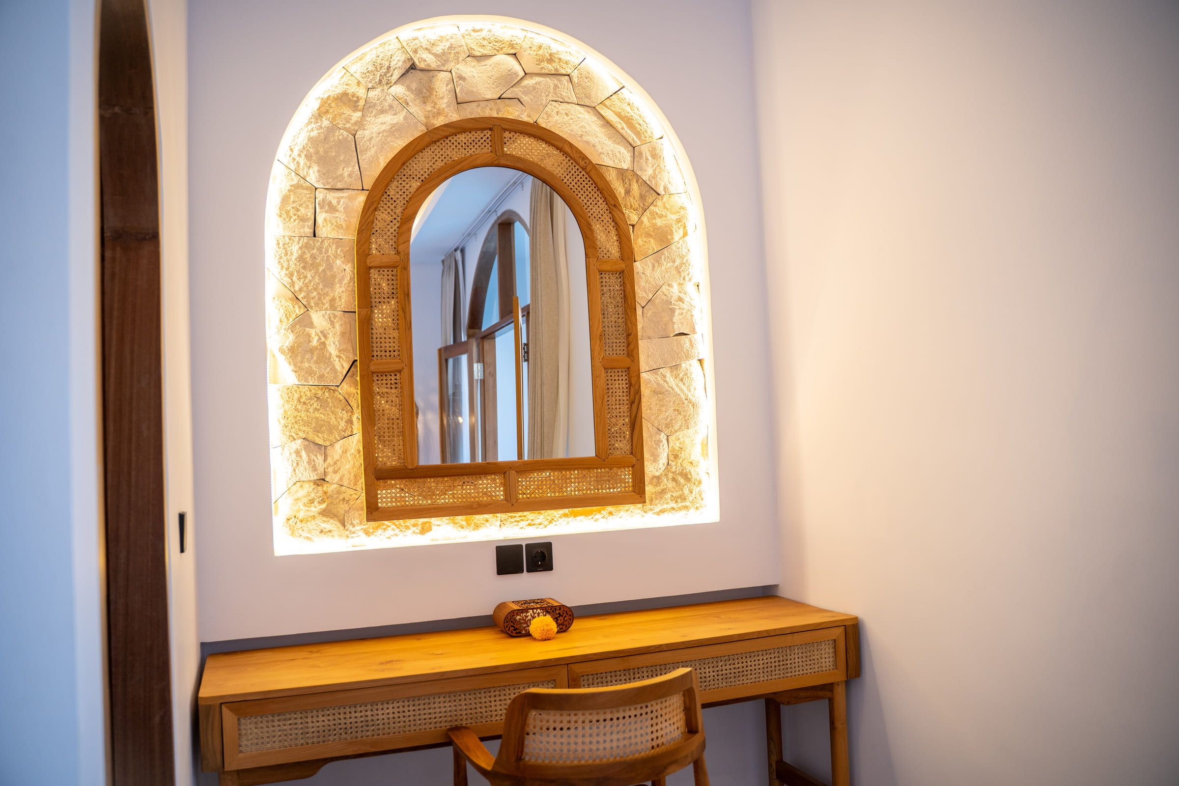 Dressing desk with a rattan chair beneath an arched mirror framed in natural stone