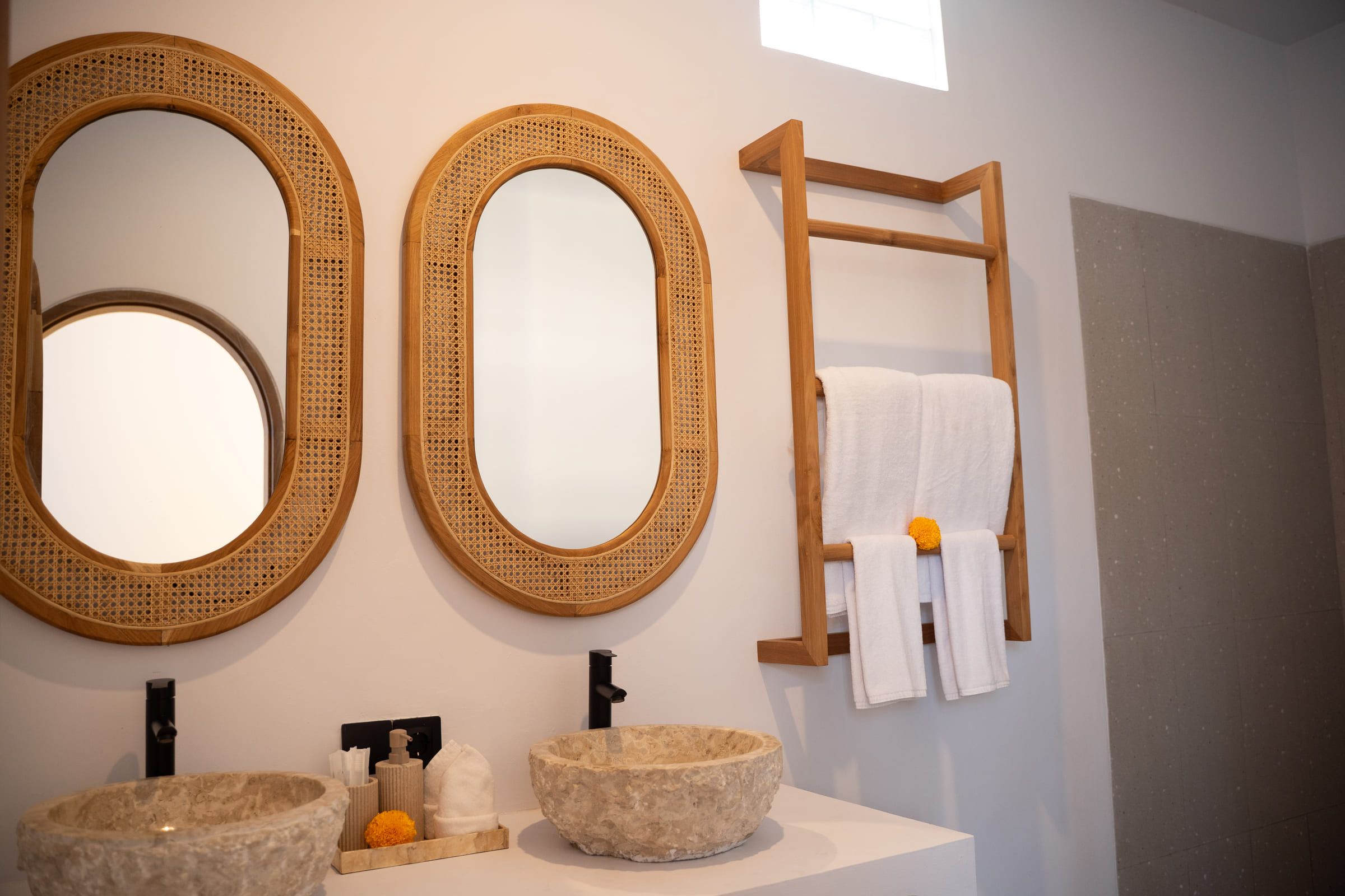 Bathroom with two oval rattan-framed mirrors, twin stone basins and a wooden towel rail