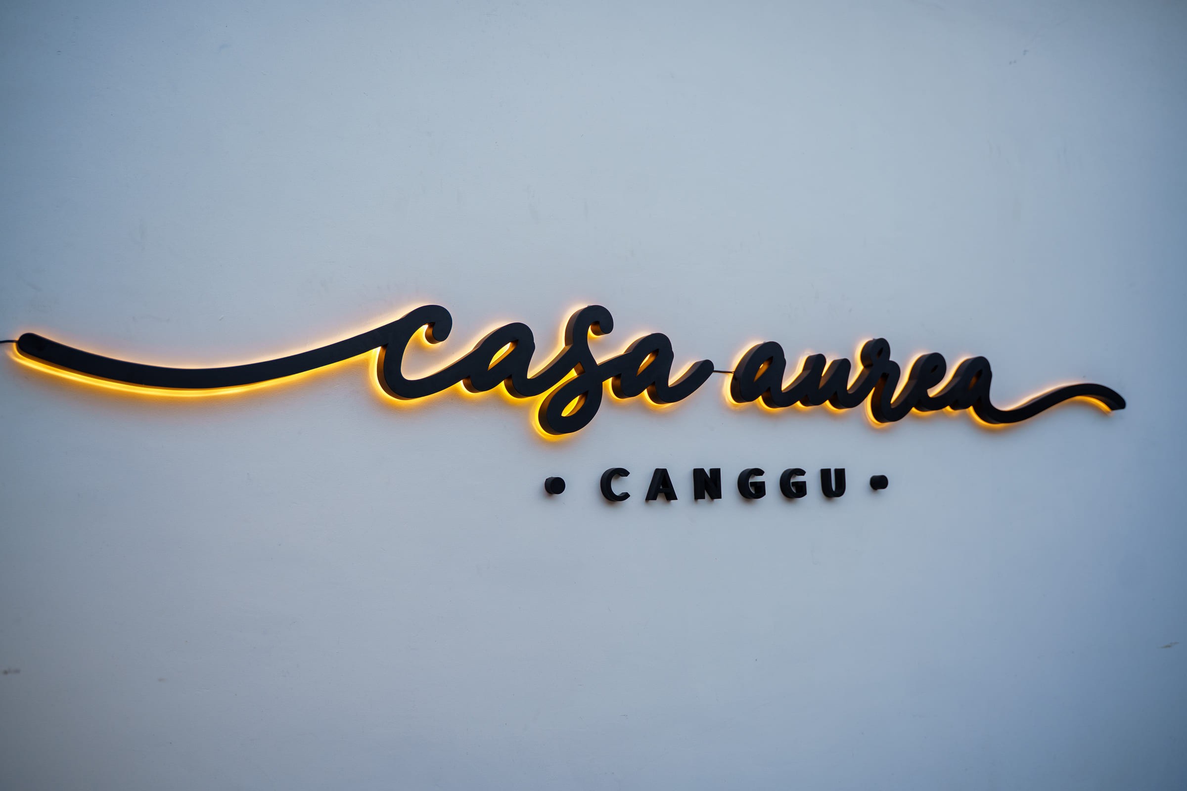 Illuminated Casa Aurea Canggu sign on a soft white wall